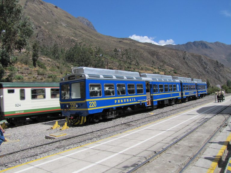 Passenger train at Ollantaytambo station beneath mountain slopes