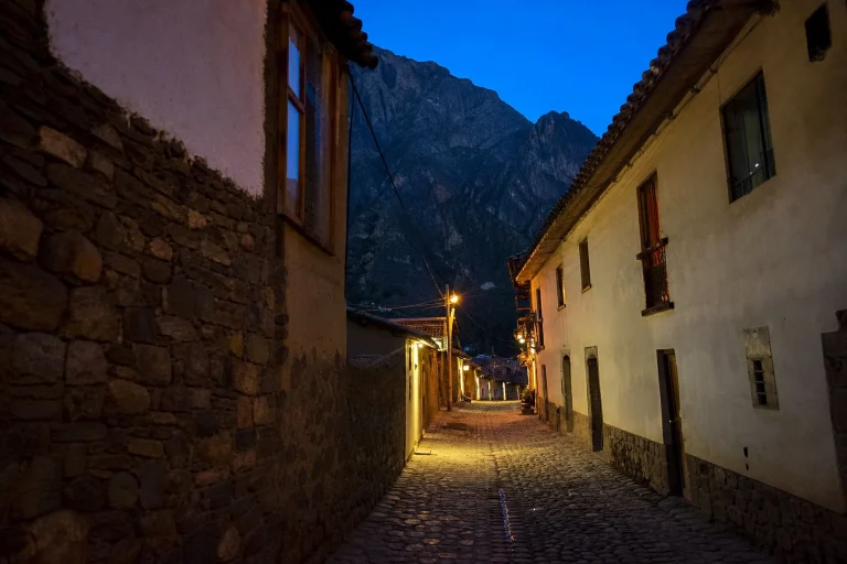 Stone-paved street in Ollantaytambo at blue hour with mountains beyond the town.